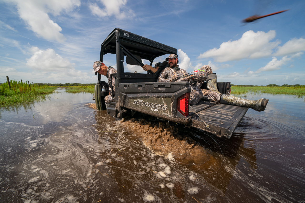 Whitetail hunters forge their way through water via a Polaris Ranger.
