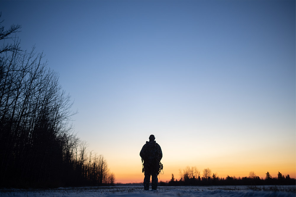 Bow hunter in the snow at sunset.