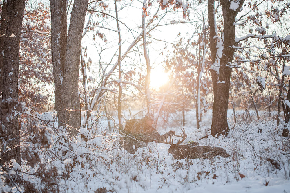 Deer hunter inspects his buck on a late season whitetail hunt in the snow. 