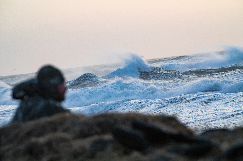 Waves crash as duck hunters attempt to shoot sea ducks from shore in high winds.